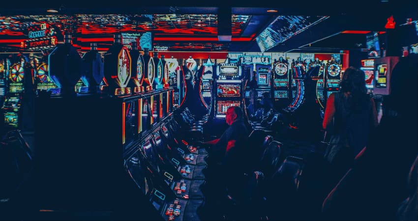 Interior of a dimly lit casino, patrons illuminated by the screens of slot machines