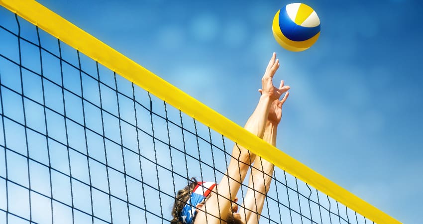 A volleyball player jumps to reach a ball flying over a net