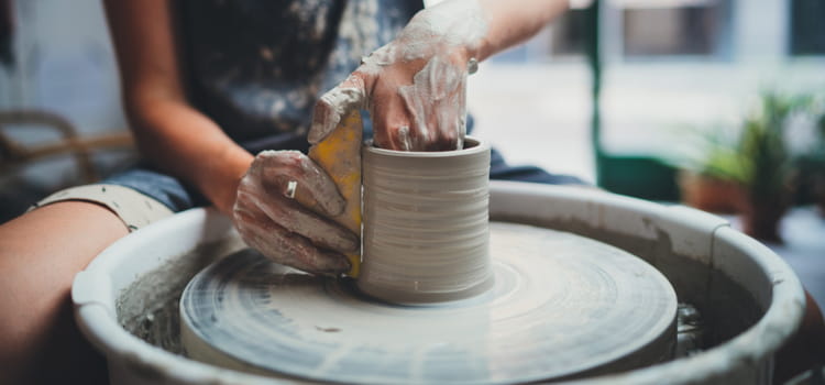 a woman shapes a pot on a pottery turntable