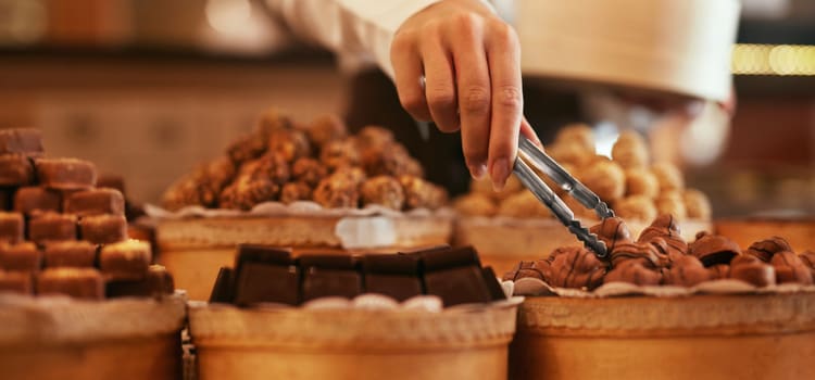 a hand holds tongs to select a dessert from an assortment of chocolates