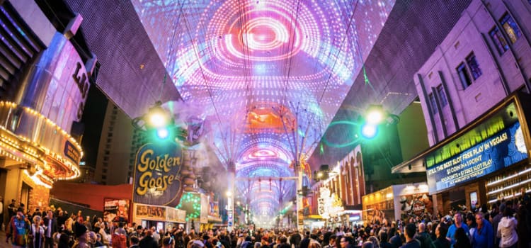 an illuminated ceiling artwork and a large crowd at night on fremont street