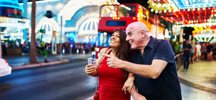 a couple smiles as they walk down an illuminated las vegas street at night