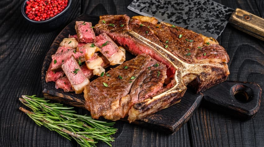 a freshly-cooked steak with small bits cut on the side and a rosemary garnish