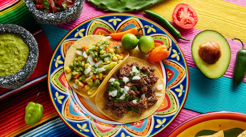 two taocs on a brightly-colored plate with a lime on the side